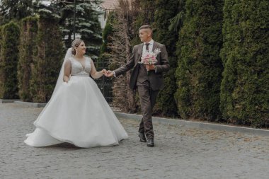 Bir gelin ve damat el ele tutuşup bir buket çiçek taşıyarak sokakta yürüyorlar. Sahne mutlu ve romantik, çünkü çift düğün günlerini kutluyor.