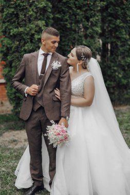 Gelin ve damat çimenli bir alanda, gelin bir buket tutuyor.