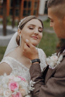Gelin ve damat birbirlerini kucaklıyor, gelin beyaz bir elbise giyiyor ve damat takım elbise giyiyor.