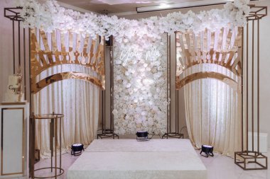 Beyaz kemerli ve beyaz duvarlı bir düğün resepsiyonu. Sahne zarif ve romantik.