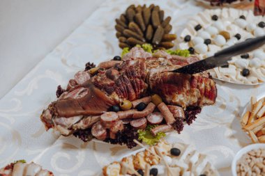 Et, sebze ve ekmek de dahil olmak üzere çeşitli yiyeceklerin olduğu bir masa. Eti kesmek için bıçak kullanılıyor.