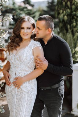 Bir erkek ve bir kadın bahçede birbirlerine sarılıyorlar. Kadın beyaz bir elbise giyiyor ve adam siyah bir gömlek giyiyor.