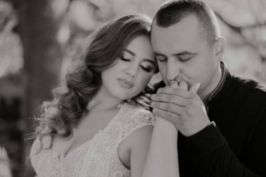 Bir erkek ve bir kadın birbirlerine sarılıyorlar. Adam siyah bir gömlek giyiyor ve kadın beyaz bir elbise giyiyor. Sahne romantik ve samimi.