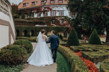 Bir gelin ve damat evin önünde bir patikadan aşağı yürüyorlar. Gelin beyaz bir elbise giyiyor ve damat mavi bir takım elbise giyiyor. Sahne huzurlu ve romantik.