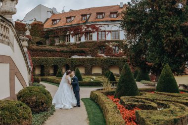 Bir gelin ve damat büyük bir evin önünde öpüşüyorlar. Evin üzerinde bir sürü sarmaşık yetişiyor.