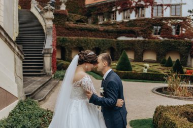 Gelin ve damat, gelinin üzerinde beyaz bir peçeyle bir binanın önünde duruyorlar. Gelin beyaz bir elbise giyiyor ve damat mavi bir takım elbise giyiyor. Birbirlerini kucaklıyorlar.