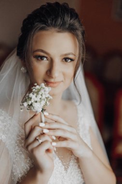 Gelinlik giyen ve elinde çiçek tutan bir kadın. Gülümsüyor ve kameraya bakıyor.
