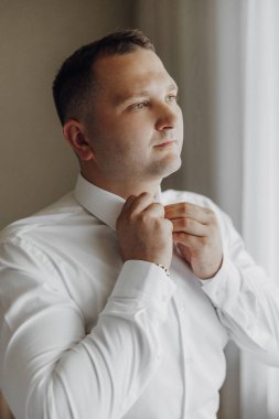 Bir adam kravatını bağlamaya hazırlanıyor. Beyaz gömlek ve siyah kravat giyiyor.