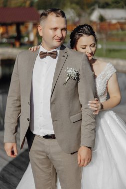 Bir adam ve bir kadın resim için poz veriyorlar. Adam takım elbise ve kravat takıyor ve kadın beyaz bir elbise giyiyor. Birbirlerine yakın duruyorlardı ve adam kadının kolunu tutuyordu.