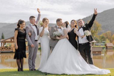 Bir grup insan bir resim için poz veriyor, bir gelin ve damat da dahil. Gelin beyaz bir elbise giyiyor ve damat da takım elbise giyiyor.