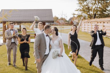 Bir gelin ve damat, siyah beyaz giyinmiş bir düğün grubuyla çevrilidir. Gelin beyaz bir elbise giyiyor ve damat bir takım elbise giyiyor. Düğün ekibi gülümsüyor.