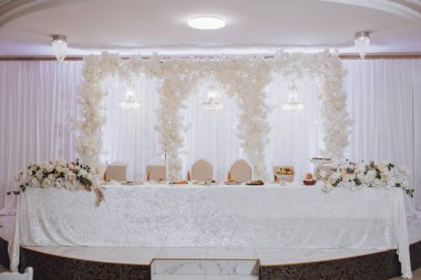 Üzerinde beyaz masa örtüsü ve beyaz çiçekler olan beyaz bir masa. Masa düğün için hazırlandı.