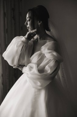 Gelinlik giymiş bir kadın duvarın önünde duruyor. Peçe takıyor ve elleri kalçasında.