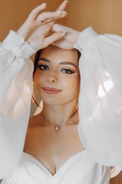 Bir kadın, kollarını açmış poz veriyor. O, beyaz bir elbise giyiyor ve saçını geri çektiriyor. Zarafet ve incelik kavramı