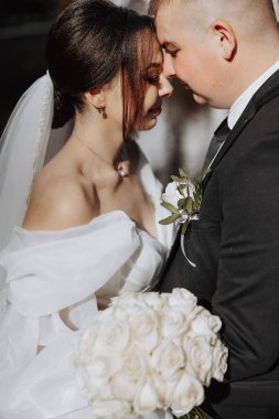 Bir gelin ve damat ellerinde bir buket beyaz gülle birbirlerini kucaklıyor. Gelin beyaz bir elbise giyiyor ve damat siyah bir takım elbise giyiyor. Aşk ve mutluluk kavramı