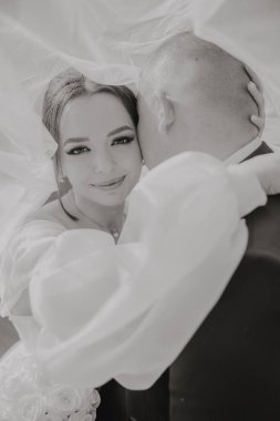 Bir gelin ve damat beyaz bir peçenin altında birbirlerini kucaklıyorlar. Gelin gülümsüyor ve damat ona bakıyor. Aşk ve mutluluk kavramı