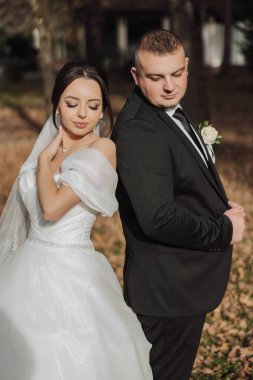 Bir gelin ve damat tarlada fotoğraf çektirmek için poz veriyor. Gelin beyaz bir elbise giyiyor ve damat siyah bir takım elbise giyiyor. Sahne mutlu ve romantik, çünkü çift düğün günlerini kutluyor.