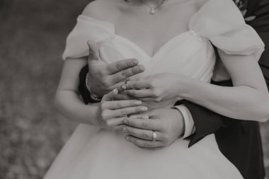 Gelin ve damat birbirlerini kucaklıyor, gelin beyaz bir elbise giyiyor ve damat takım elbise giyiyor.