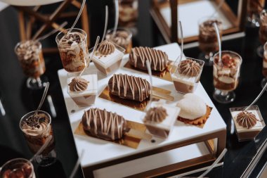 Pasta ve pastalar da dahil olmak üzere tatlılarla dolu bir masa bir parti için hazırlanıyor. Tatlılar küçük bardaklarda ve kaselerde düzenleniyor, ve misafirlerin kullanabileceği kaşıklar var.