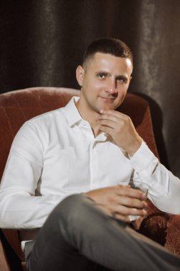 Beyaz gömlekli bir adam elleri çenesinde bir sandalyede oturuyor. Gülümsüyor ve rahatladı.