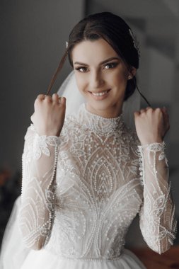 Bir kadın uzun bir tren ve duvağı olan beyaz bir gelinlik giyiyor. Gülümsüyor ve kameraya poz veriyor.