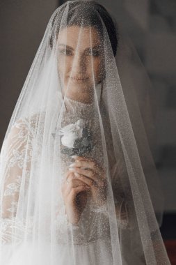 Bir kadın peçe takıyor ve elinde bir çiçek tutuyor. Duvak beyaz ve yüzünü örtüyor.