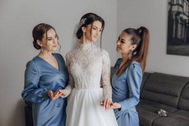 Üç kadın bir odada dikiliyor, biri gelinlik giyiyor. Diğer iki kadın mavi giyinmiş ve onun arkasında ellerini tutuyorlar. Sahne kutlamalardan biridir.