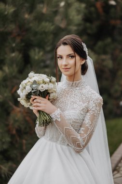 Beyaz gelinlik giyen bir kadın elinde bir buket çiçek tutuyor. Yüzünde güzel bir gülümseme var ve buketteki çiçekler beyaz. Mutluluk ve kutlama kavramı