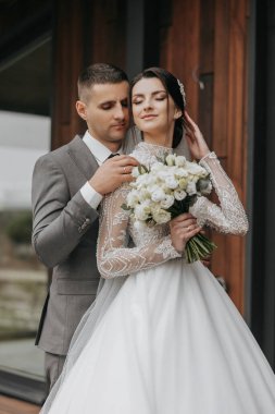 Bir gelin ve damat bir buket beyaz çiçekli bir resim için poz veriyorlar. Gelin beyaz bir elbise giyiyor ve damat bir takım elbise giyiyor. Sahne mutlu ve romantik.