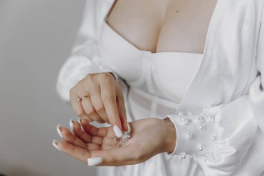 Bir kadın beyaz bir elbise giyiyor ve elinde küçük bir elmas yüzük tutuyor. Zarafet ve entelektüellik kavramı, kadın resmi bir kıyafet giydiği için.