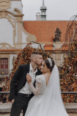 Bir adam ve bir kadın bir binanın önünde öpüşüyorlar. Adam takım elbise giyiyor ve kadın da gelinlik giyiyor. Sahne romantik ve samimi.