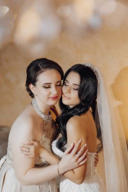 İki kadın birbirine sarılıyor, bir tanesi gelinlik giyiyor. Sahne sıcak ve sevgi dolu.