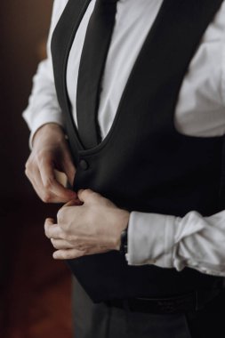 Siyah takım elbiseli ve beyaz gömlekli bir adam kravatını düzeltiyor. Formalite anlayışı ve detaylara dikkat, adam kravatını dikkatlice düzeltirken,