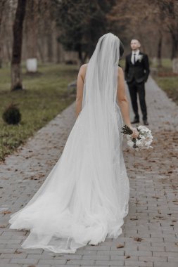 Gelin ve damat tuğla bir yolda yürüyorlar, gelin beyaz bir elbise ve duvak takıyor.