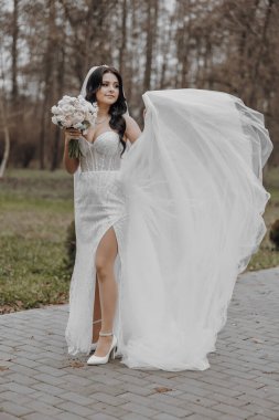 Beyaz gelinlikli bir kadın elinde bir buket çiçek tutuyor. O bir tuğla kaldırımda duruyor ve elbisesi arkasında akıyor. Zarafet ve kutlama kavramı