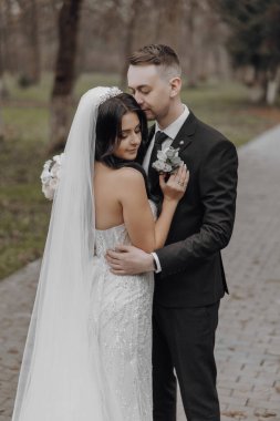 Bir gelin ve damat tuğla bir yolda birbirlerine sarılıyorlar. Damat siyah bir takım giyerken gelin beyaz bir elbise ve duvak takıyor. Çift mutlu ve aşık görünüyor.