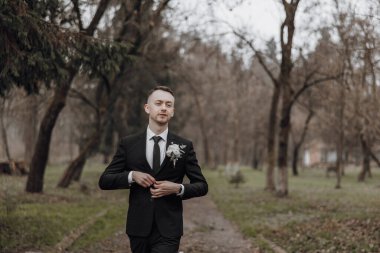 Takım elbiseli bir adam elinde bir buket çiçekle parkta yürüyor. Sahne sakin ve huzur dolu. Uzağa bakan adamla birlikte.