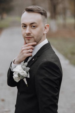 Takım elbiseli ve kravatlı bir adam yakasında yaka çiçeğiyle fotoğraf için poz veriyor.