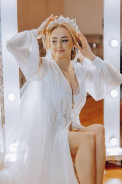 Beyaz elbiseli bir kadın aynanın önünde oturuyor. O bir taç takıyor ve saçları topuz şeklinde. Zarafet ve entelektüellik kavramı. Kadın özel bir durum için giyinmiş.