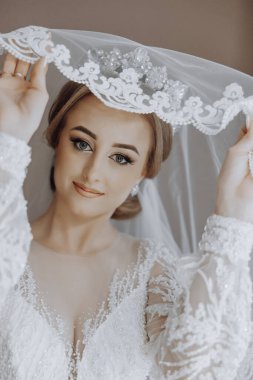 Bir kadın beyaz bir peçe takıyor ve gülümsüyor. O bir gelinlik giyiyor ve bir resim için poz veriyor.