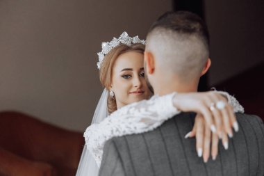 Bir gelin ve damat birbirlerini kucaklıyor. Gelin taç takıyor ve damat da alyans takıyor.