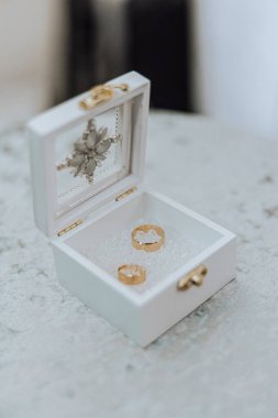 İçinde iki altın yüzük olan beyaz bir kutu. Kutu bir çiçek tasarımı ile süslenmiş.