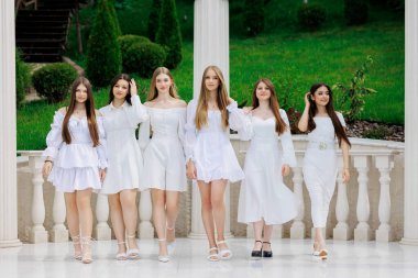 Bir grup genç kadın beyaz giyinmiş ve sırada bekliyorlar. Hepsi gülümsüyor ve bir resim için poz veriyor gibi görünüyorlar. Manzara neşeli ve dostane.