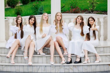 Bir grup genç kadın bir dizi basamakta oturuyor, hepsi de beyaz elbiseler giyiyor. Bir resim için poz veriyorlar, ve görüntünün havası dostluk ve arkadaşlıktan ibaret.