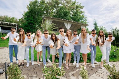 Parkta fotoğraf çektirmek için poz veren bir grup genç. Sahne neşeli ve eğlenceli, grup gülümsüyor ve eğleniyor.