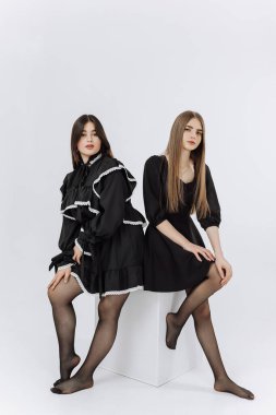 Siyah elbiseli iki kadın fotoğraf için poz veriyor. Sahne zarif ve sofistike.