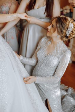 Bir kadın düğüne hazırlanıyor ve başka bir kadın ona yardım ediyor. Gelin beyaz bir elbise giyiyor ve diğer kadın gümüş bir elbise giyiyor. Sahne desteklerden biridir.