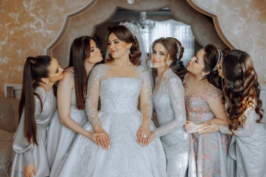 Bir grup kadın, ortasında bir gelin olan bir fotoğraf için poz veriyor. Gelin beyaz bir elbise giyiyor ve arkadaşları tarafından çevrili. Sahne mutlu ve kutlama dolu.