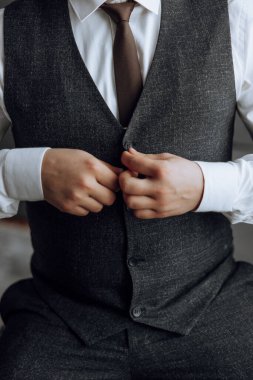 Siyah yelek ve beyaz gömlekli bir adam kravatını düzeltiyor. Formalite ve detaylara dikkat etme kavramı, adamın görünüşünün parlak ve profesyonel olması için özen göstermesi gibi.