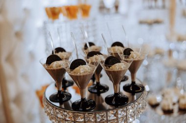 Birkaç bardak çikolata ve yulaflı kurabiye de dahil olmak üzere çeşitli tatlıların olduğu bir masa. Tatlılar berrak bardaklarda sunuluyor ve siyah bir tepside diziliyorlar.